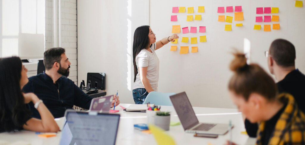 Staged picture of a group of people in a meeting room in front of a board with notes on it.